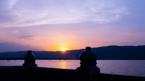 A sun setting over a mountain filling the sky with pink hues