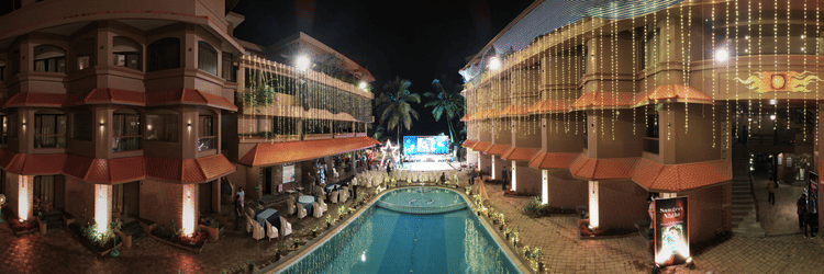 The exterior of Uday Samudra Leisure Beach Hotel at night, with vibrant lighting hanging from the building’s roof, illuminating the pool and creating a festive celebration vibe