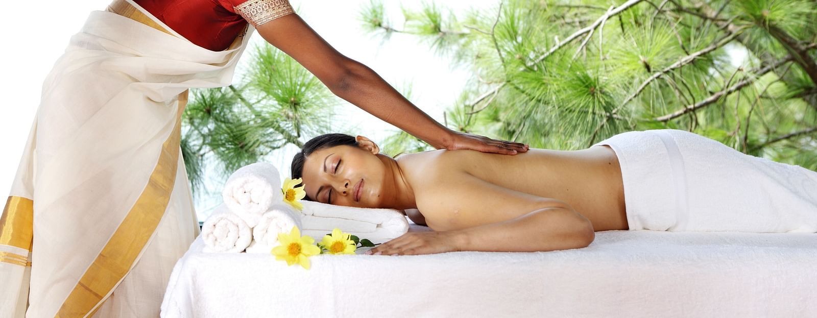 A woman lies on a spa table while another woman massages her back, in an outdoor environment