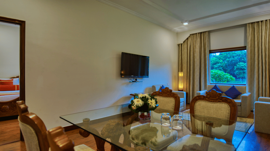 An Premium Suite living space at Clarks Khajuraho featuring seating, a dining table setup, a television, and a window allowing natural light.