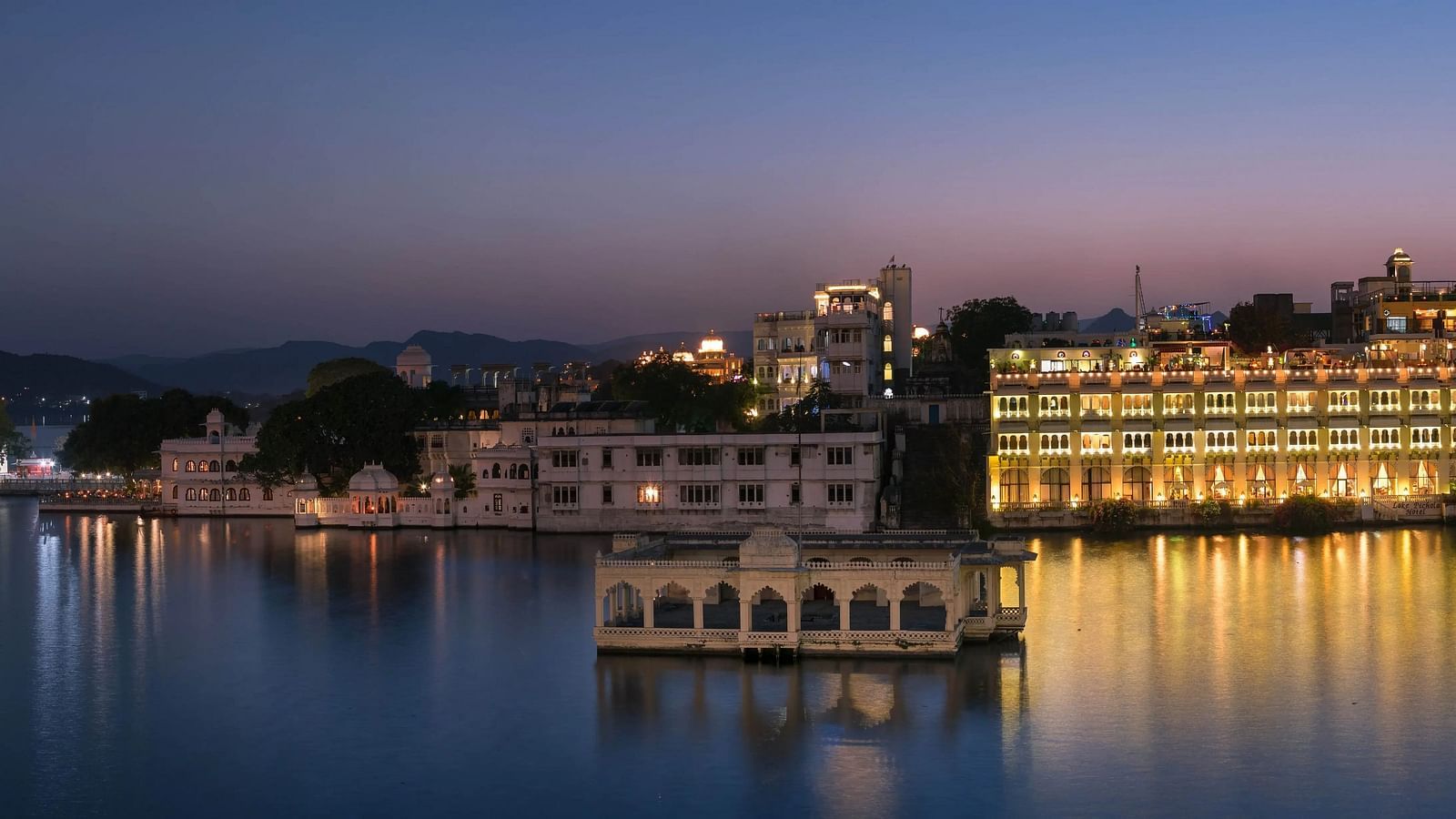 A lit palace reflects in water at dusk, with sky and hills.