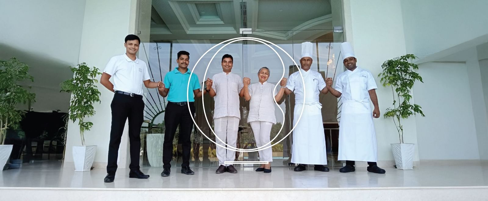 The staff members of Miros Hotels standing together holding each others hands in a brightly lit lobby.