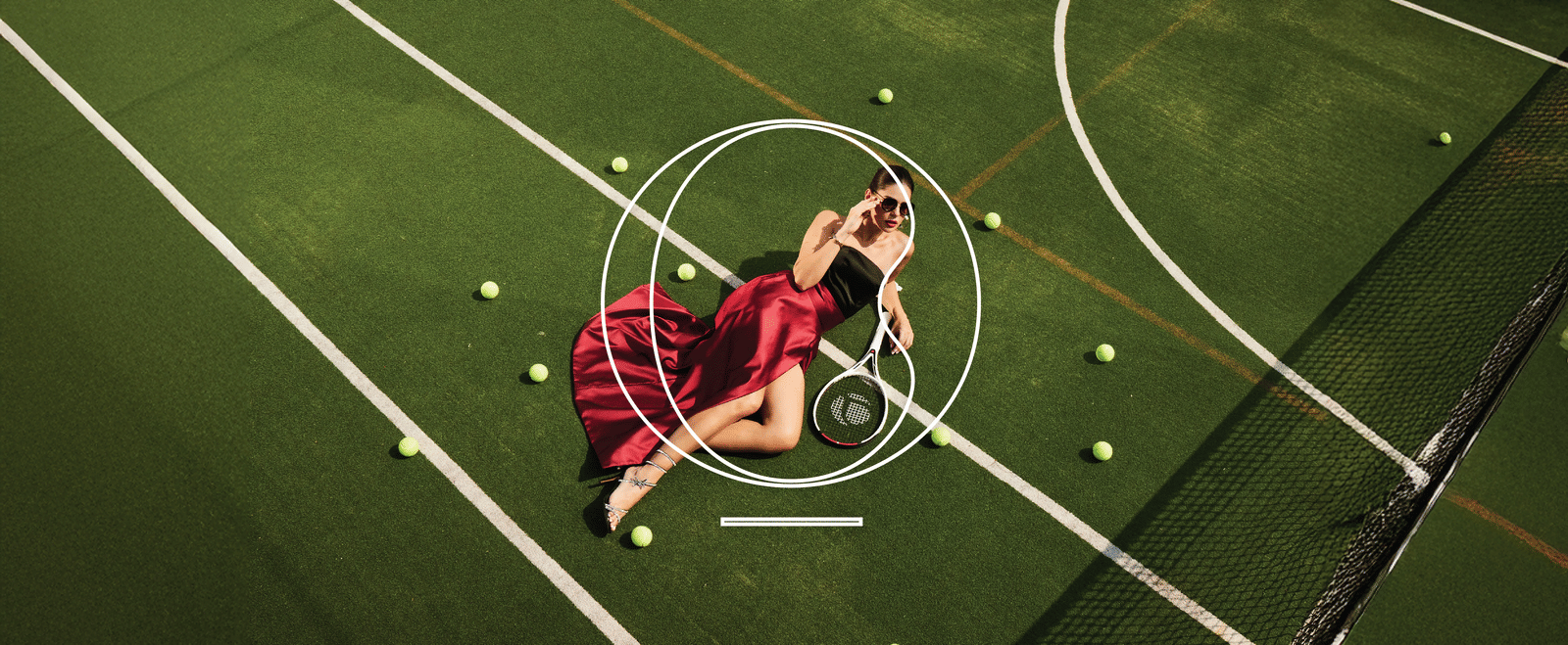 A woman wearing a maroon satin dress lying down on a grass field with a tennis racket at Miros Hotels, one of the best activities in North Goa to experience.