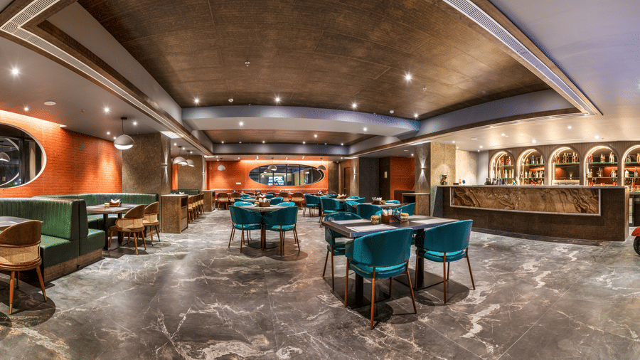 A wide-angle shot of the Distil Bar showing contemporary teal and yellow arm chairs arranged around marble-topped tables under warm, recessed lighting – Skkylight Lords Inn, Nanded