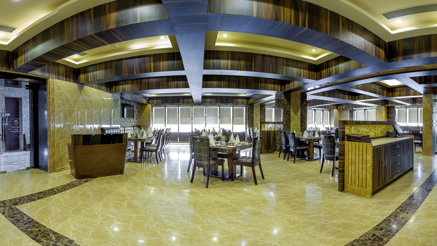 Spacious modern restaurant interior featuring polished marble floors, dark wooden tables, and decorative recessed ceiling lighting at Golden Tulip Kukas, Jaipur.