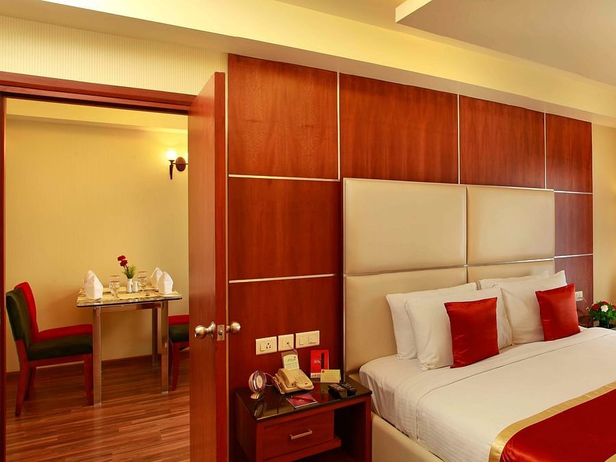 A stylish bedroom with a king-size bed, wooden accents, and an adjoining dining area, exuding luxury and comfort. - La Classic, Hosur Road
