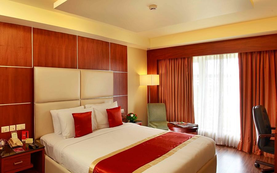 A stylish bedroom with a king-size bed, wooden accents, and an adjoining dining area, exuding luxury and comfort. - La Classic, Hosur Road