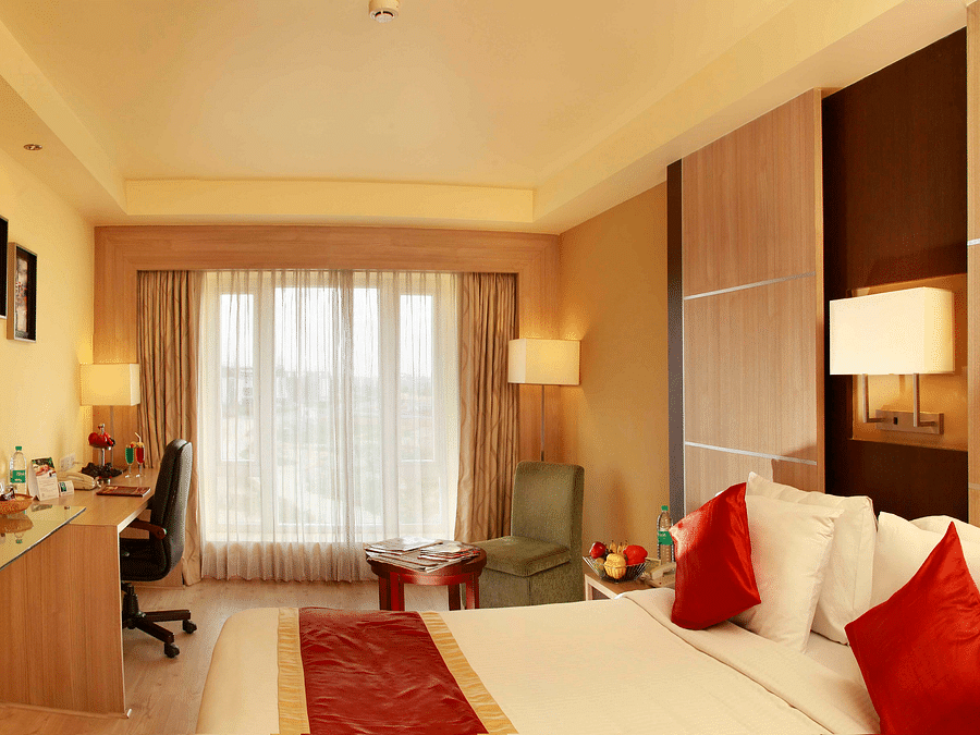 A cosy hotel room with elegant interiors, a work desk, a mounted TV, and a large window with soft curtains. - La Classic, Hosur Road