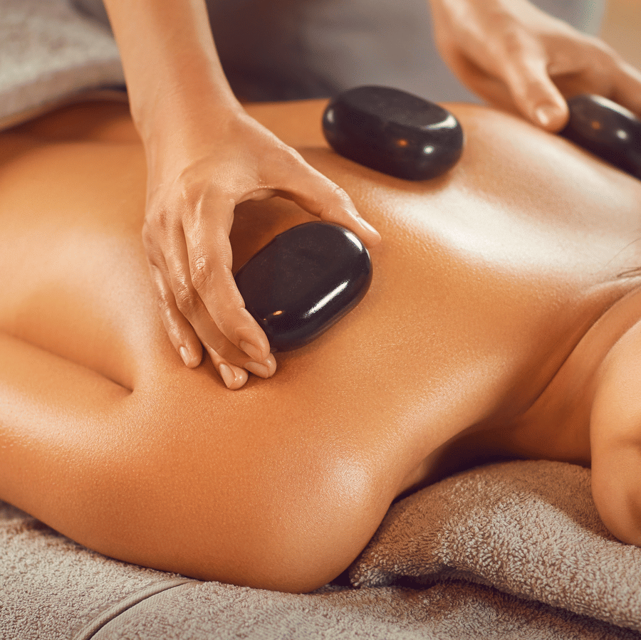 Relaxing hot stone massage therapy on a woman’s back besides burning candles.