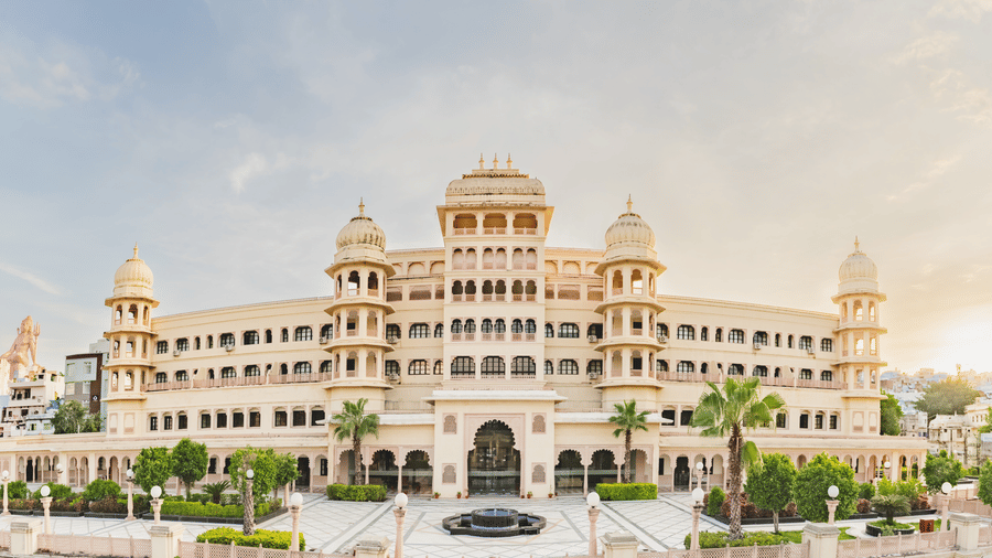 Panaromic view of Shri Vallabh Vilas Lords Plaza Nathdwara, featuring arched windows, domes, lush green gardens and a central fountain.
