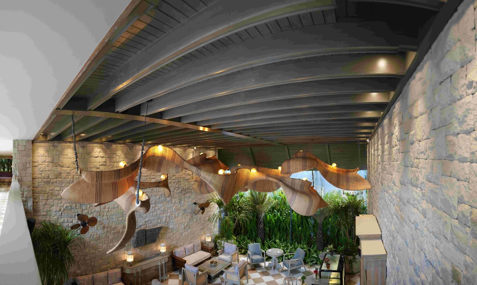 A wide-angle shot of the charming Suenos de Cafe at The Evren, Vagator, featuring a chequered floor, well-arrnaged seating, and a striking, large, woven light fixture.