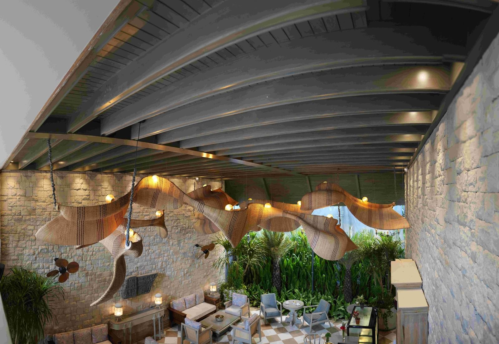 A wide-angle shot of the charming Suenos de Cafe at The Evren, Vagator, featuring a chequered floor, well-arrnaged seating, and a striking, large, woven light fixture.