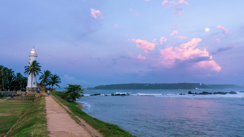 an evening view of a lighthouse located on the shore of a beach