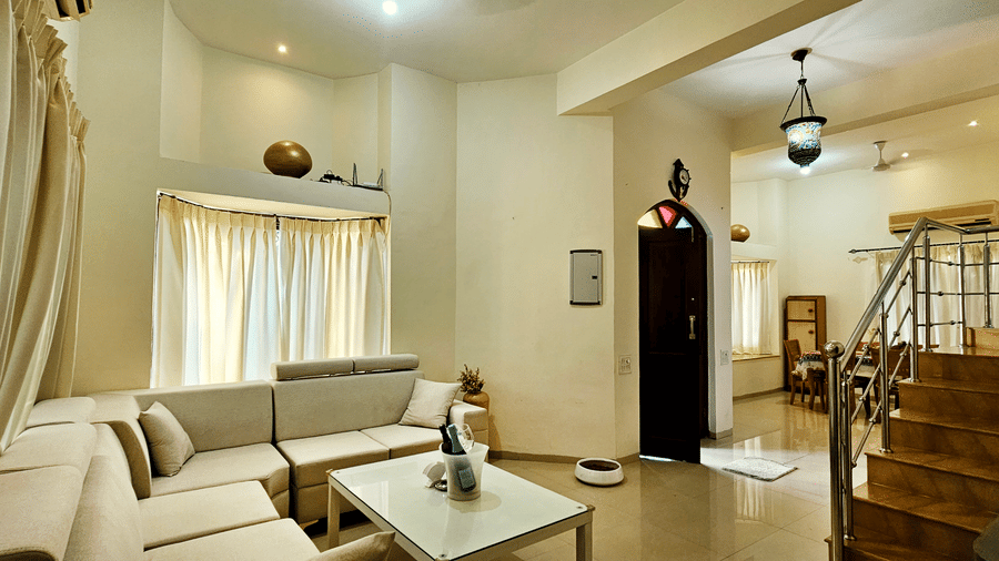 A wide-angle shot of the living area featuring the plush couch set along with the staircase in the corner at Amara Villa, Nagoa.