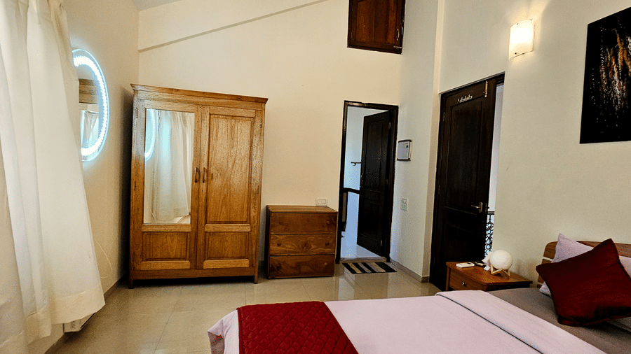 Side view of a bedroom at Amara Villa, Nagoa, featuring a wooden wardrobe along with a double bed in a room with high ceiling.