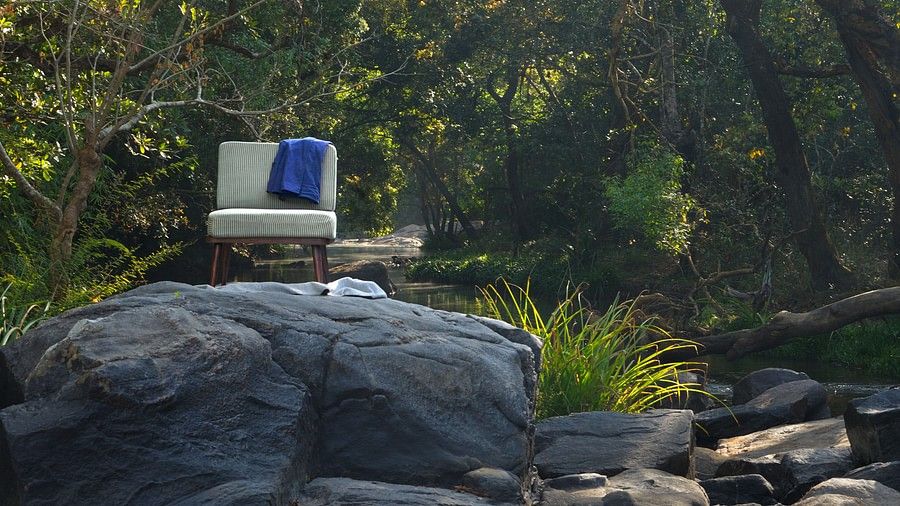Sofa chair set up on a rock in a natural setting with trees and flowing water.