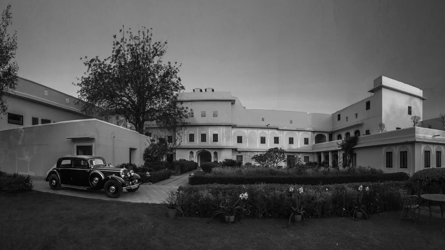 A black and white photo of a building and vintage cars parked outside Royal Heritage Haveli.