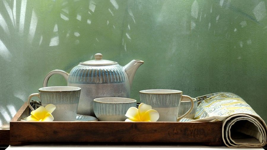 Tea set with a striped teapot, cups, and yellow flowers on a tray in front of a window