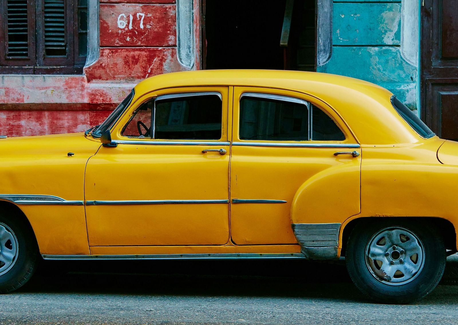 A yellow taxi parked near the side walk with a person sitting on steps behind the car.