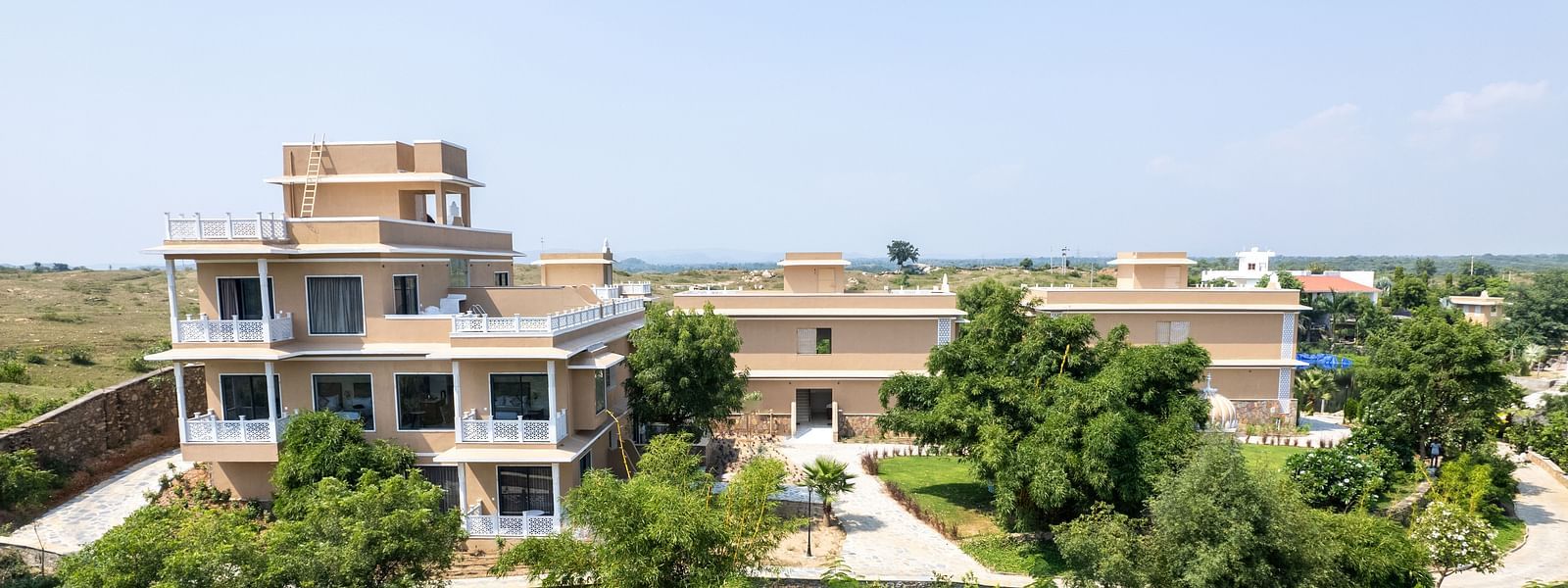 An aerial shot a facade in between lush greenery seen on a sunny day - Rajbagh Wellness, Udaipur.