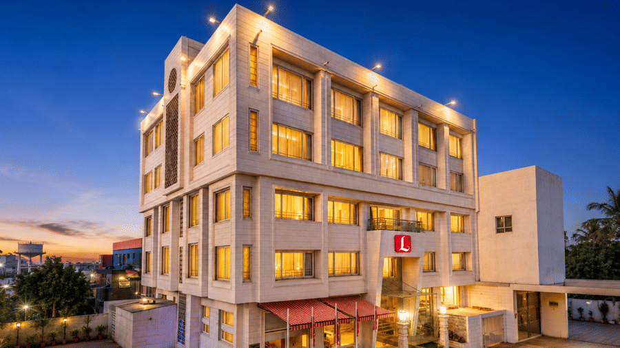 Exterior view of Dwarkadhish Lords Eco Inn at dusk featuring a multi-story modern hotel building with warmly lit windows against a twilight sky.