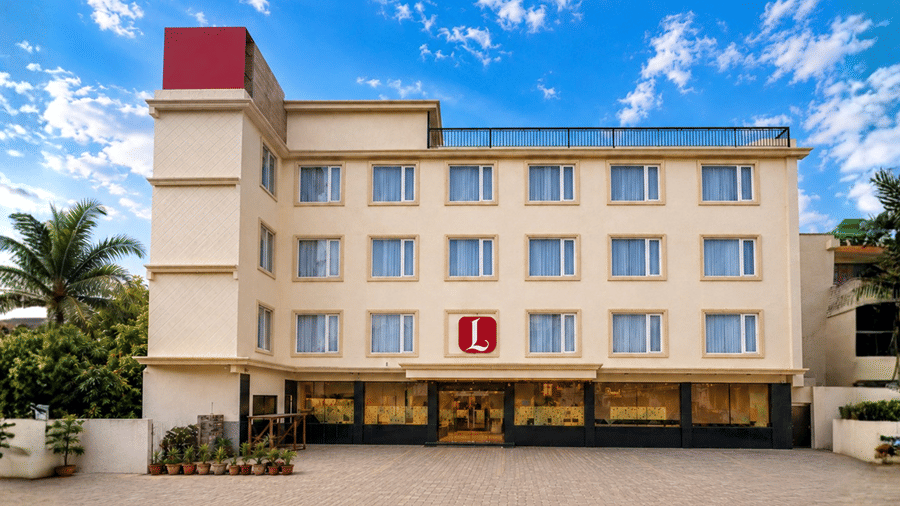 Exterior view of Lords Inn Katra featuring a multi-story hotel building with bright windows, a prominent red logo on the front facade, and a clear blue sky.