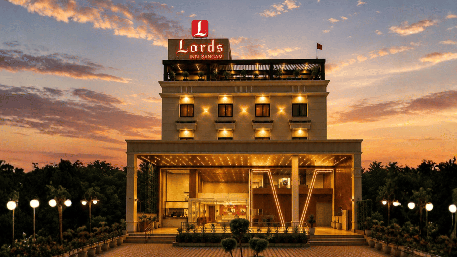 Exterior sunset view of Lords Inn Sangam Bhopal featuring a brightly illuminated multi-story building facade, rooftop logo, warm entrance lighting, and a dusk sky.