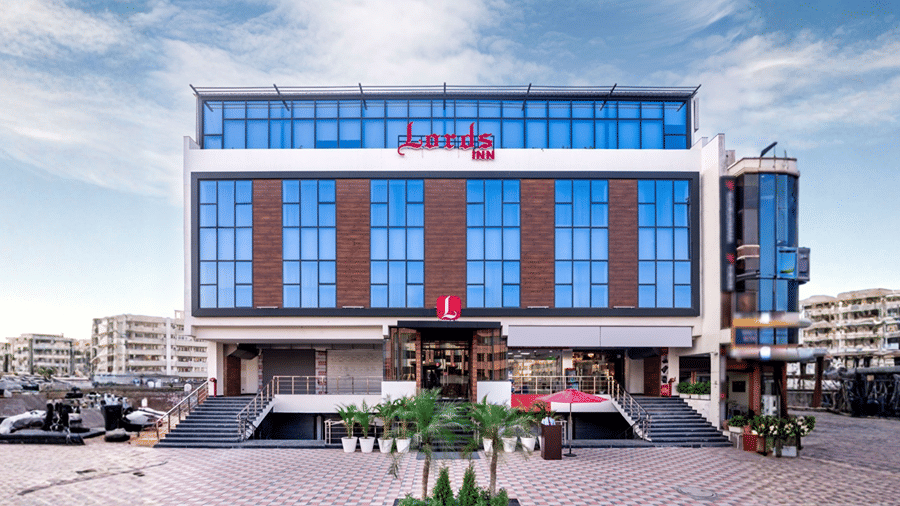 Front exterior view of Lords Inn Zirakpur featuring a multi-story modern building with blue tinted glass windows, wood-panel accents, central entrance ramp, and red signage.