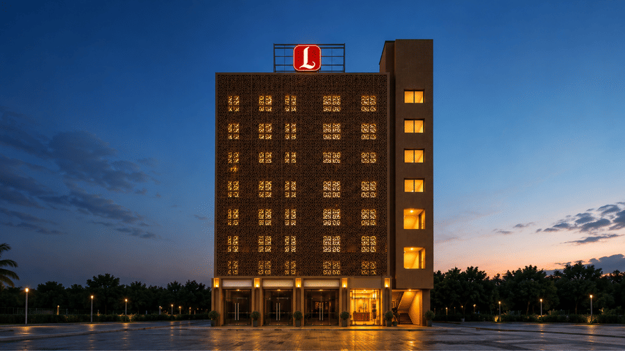 Exterior view of an illuminated multi-story SK Lords Inn Ahmedabad building at dusk with a prominent red rooftop logo and warm lighting across the windows and ground floor.