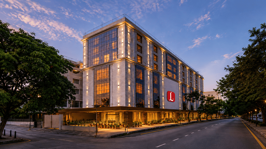 Modern multi-story exterior of Skkylight Lords Inn, Nanded illuminated at twilight, featuring vertical lighting, large glass windows, a red brand logo, and a street view.