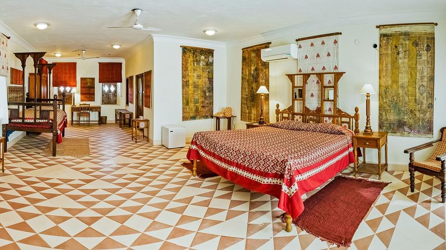 Large bedroom with a bed, wooden furniture, patterned tile flooring, windows with curtains, and a seating area at Tijara Fort-Palace - 19th Century, Alwar.