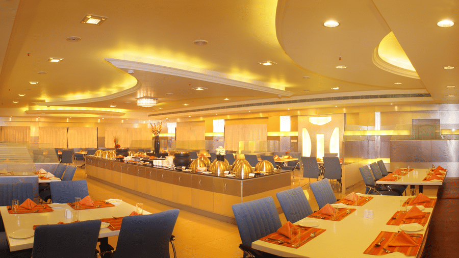 Kanni Restaurant at DSF Grand Plaza, Tuticorin with a long gold buffet counter, dining tables set with orange napkins, and warm ambient lighting.