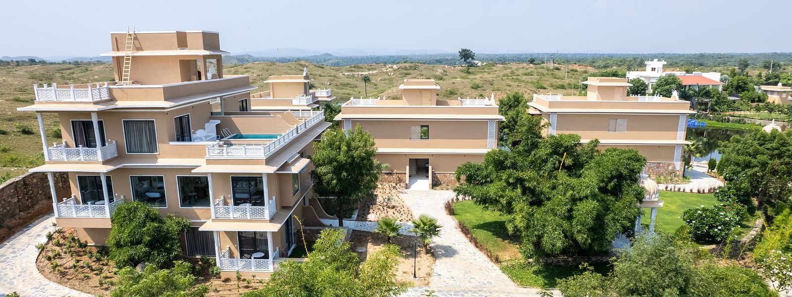 An aerial shot a facade building in between lush greenery seen on a sunny day - Rajbagh Wellness, Udaipur