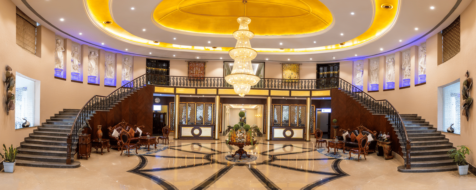 Panoramic view of a grand hotel lobby with a sweeping double staircase, marble floors, and a huge central chandelier at Hotel Hukam's Lalit Mahal.