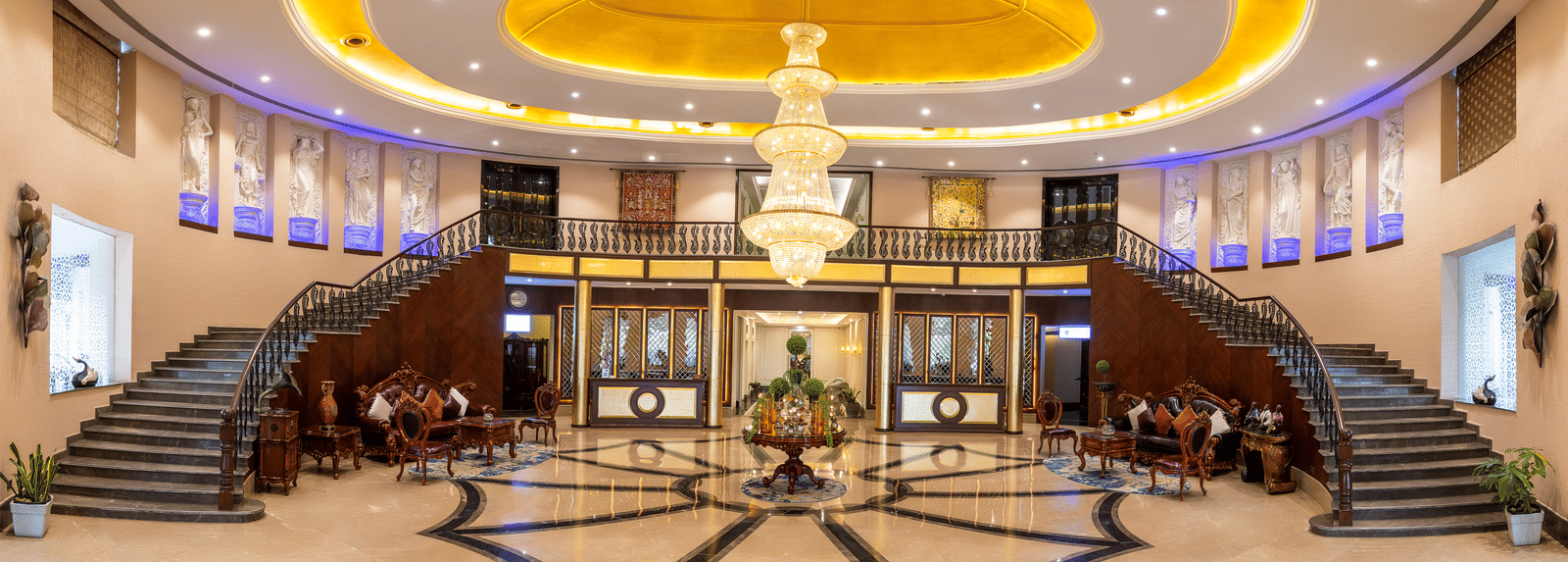 Panoramic view of a grand hotel lobby with a sweeping double staircase, marble floors, and a huge central chandelier at Hotel Hukam's Lalit Mahal.