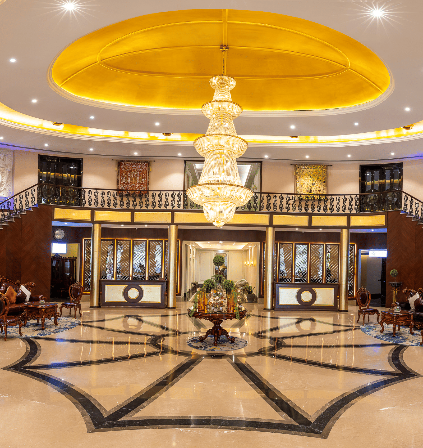 Panoramic view of a grand hotel lobby with a sweeping double staircase, marble floors, and a huge central chandelier at Hotel Hukam's Lalit Mahal.