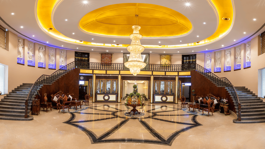 Panoramic view of a grand hotel lobby with a sweeping double staircase, marble floors, and a huge central chandelier at Hotel Hukam's Lalit Mahal.