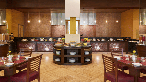 A restaurant dining hall with rows of tables and chairs arranged around a central buffet counter at The Retreat Hotel & Convention Centre.
