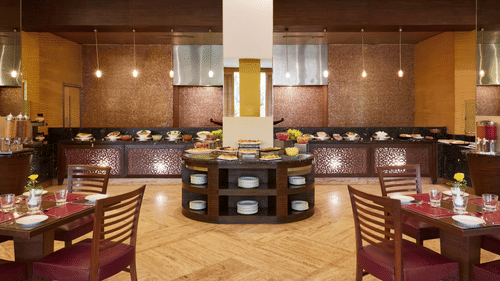 A restaurant dining hall with rows of tables and chairs arranged around a central buffet counter at The Retreat Hotel & Convention Centre.