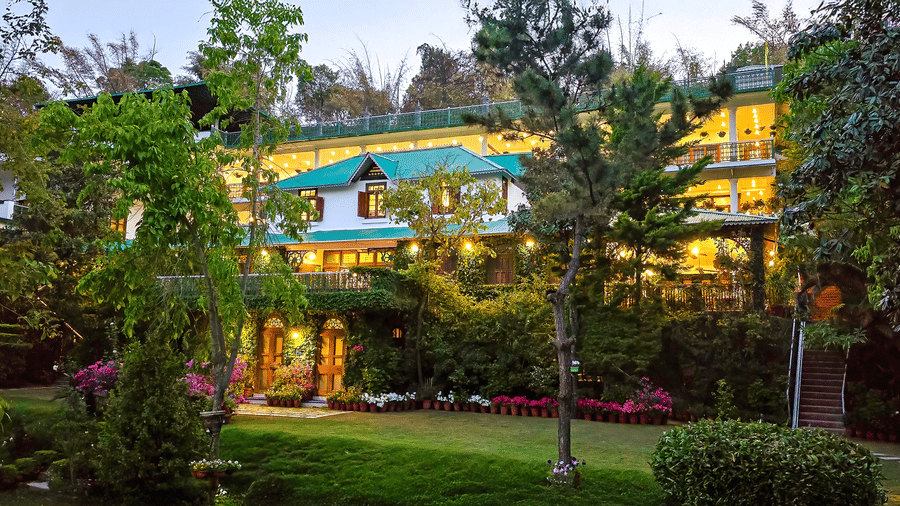 Facade of Shaheen Bagh, the best hotel in Dehradun with a swimming pool, with warm lights and trees and flowers surrounding the building.