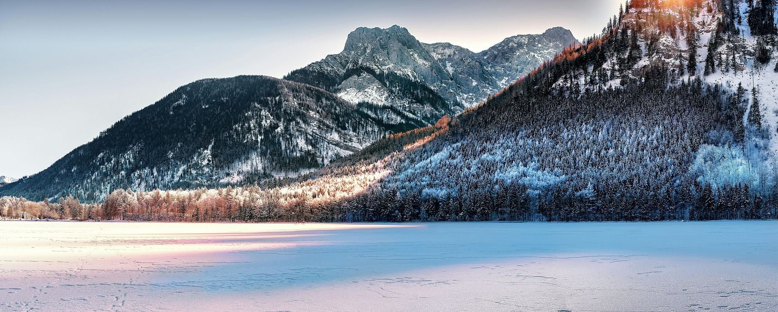 Sunlight glints off snow-dusted mountains overlooking a vast, frozen white expanse.