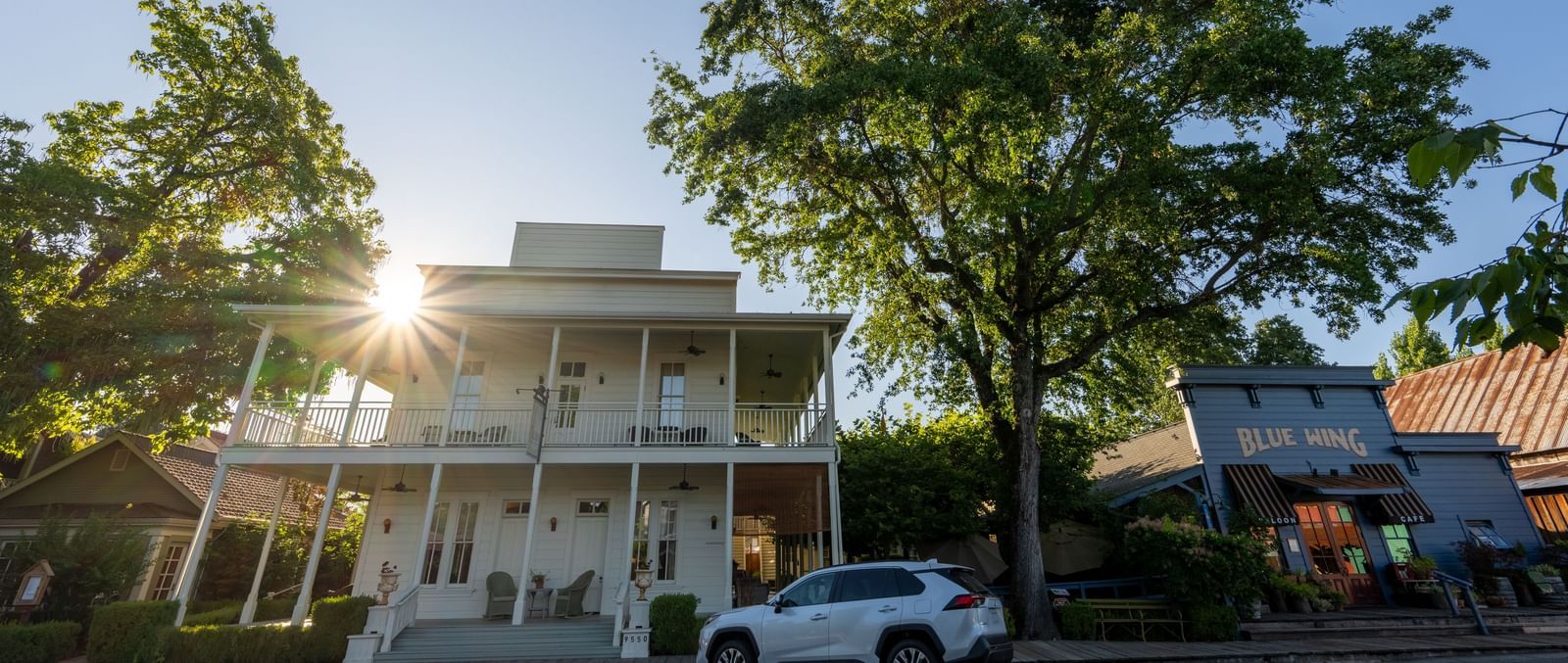 The stately white hotel building stands proudly with green trees under a clear sky at The Tallman Hotel.