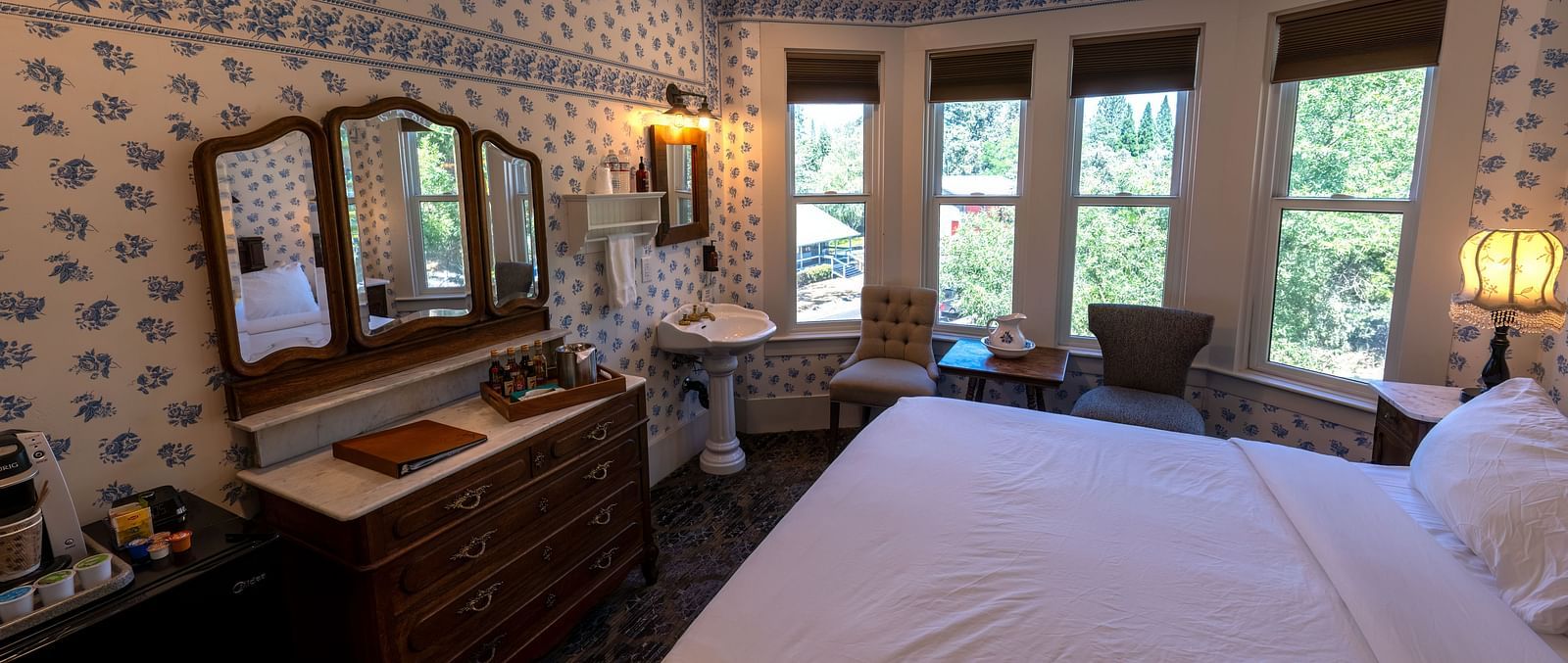 Cosy guest room with patterned wallpaper, wooden vanity and ample sunlight at The Groveland Hotel.