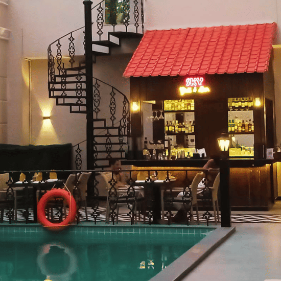 Cocktail counter at the poolside bar with purple LOVE neon, drinks lineup, hookah, and spiral staircase behind the wood-framed bar at Polo Hotel, Agartala.