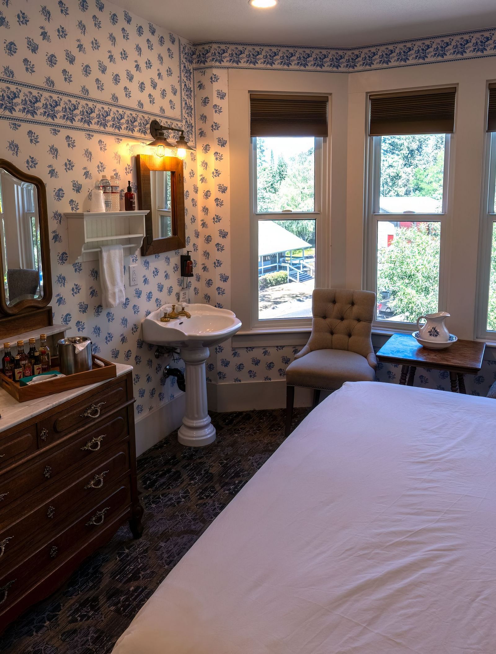 Cosy guest room with patterned wallpaper, wooden vanity and ample sunlight at The Groveland Hotel.