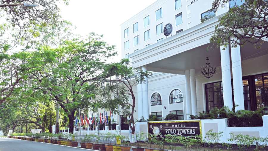 Polo Hotel, Agartala main entrance with white columned porte-cochere, signage reading HOTEL POLO TOWERS, flags and tree-lined driveway.