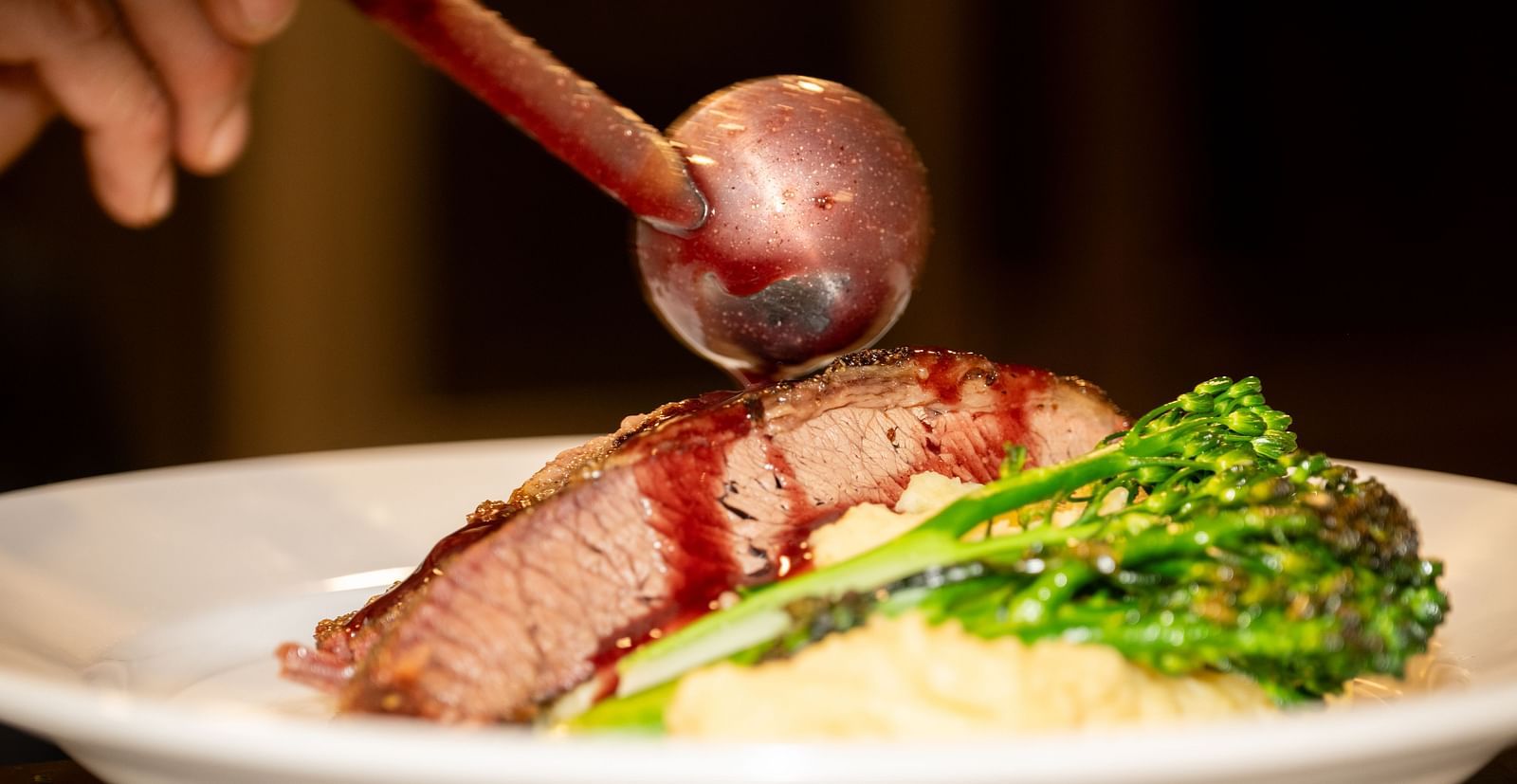 A gourmet steak dish being plated with mashed potatoes and greens at The Groveland Hotel.