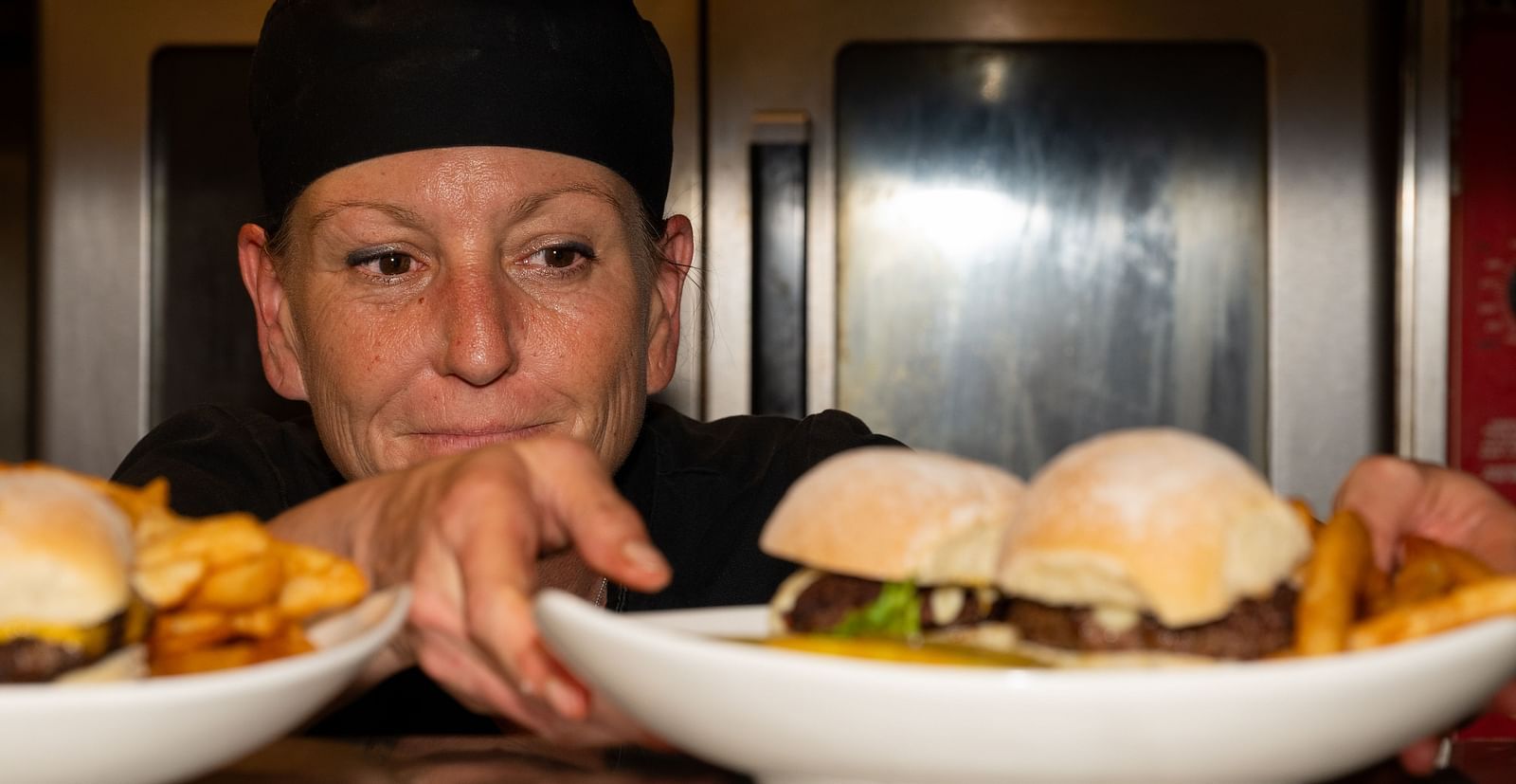 Chef presenting plates of sliders and chips from the kitchen pass at The Groveland Hotel.