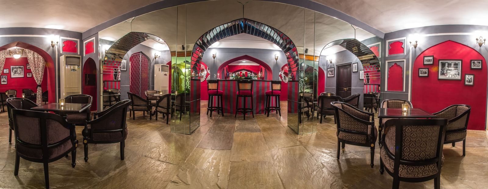 A long, arched dining hall with tables and chairs, illuminated, within Royal Heritage Haveli.
