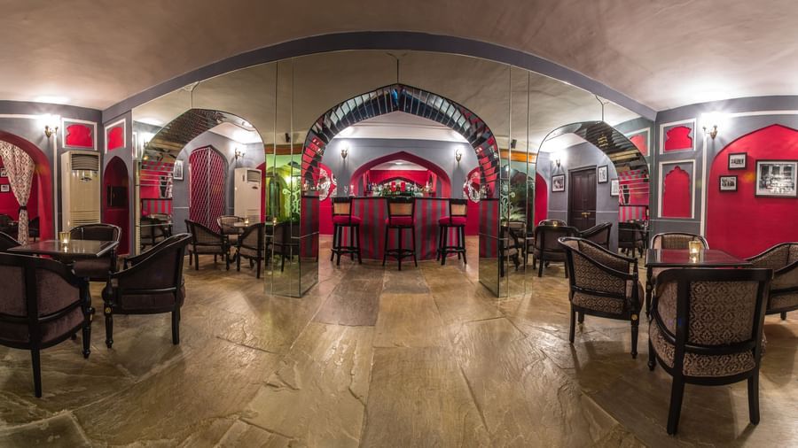 A long, arched dining hall with tables and chairs, illuminated, within Royal Heritage Haveli.
